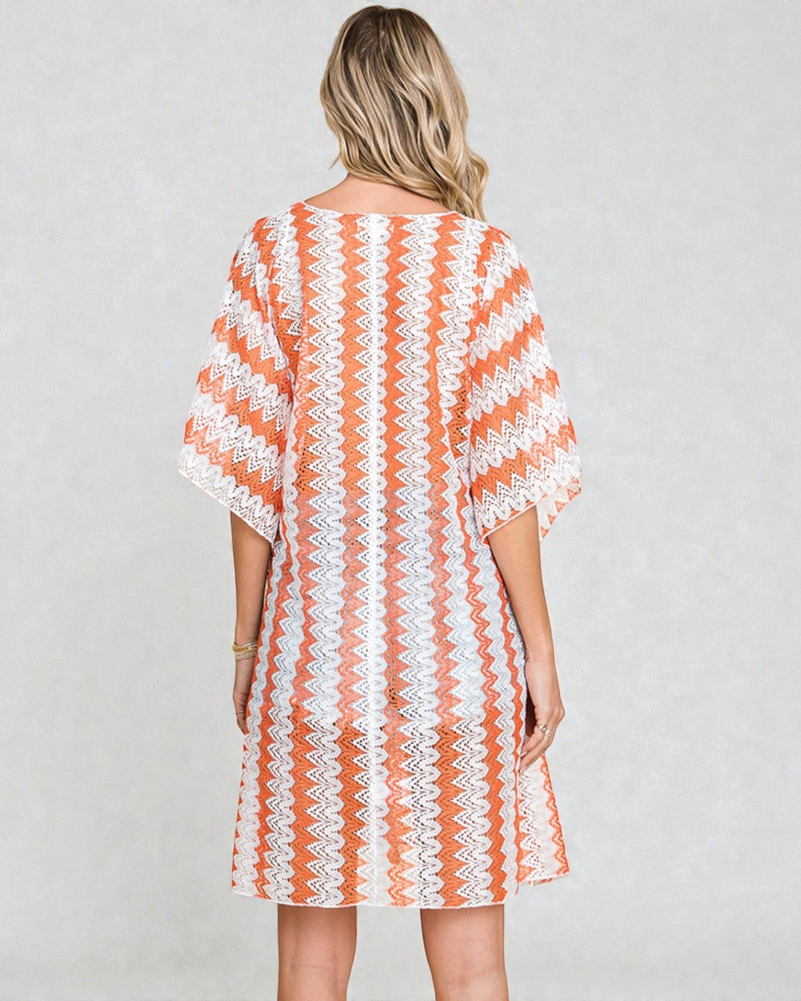 Woman wearing a orange and white patterned dress on a plain background