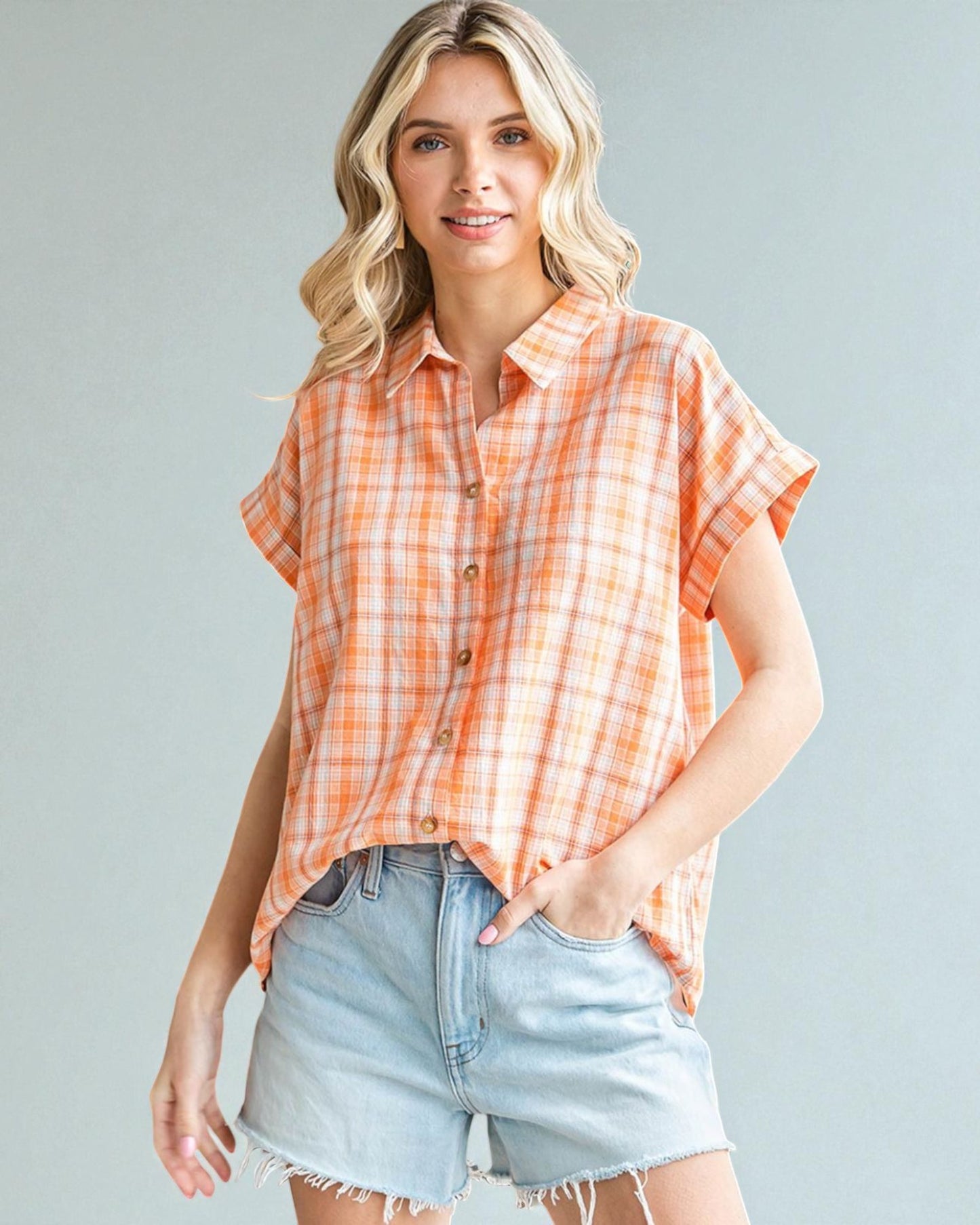 Woman wearing an orange plaid shirt and denim shorts against a gray background