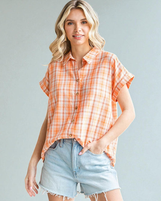 Woman wearing an orange plaid shirt and denim shorts against a gray background