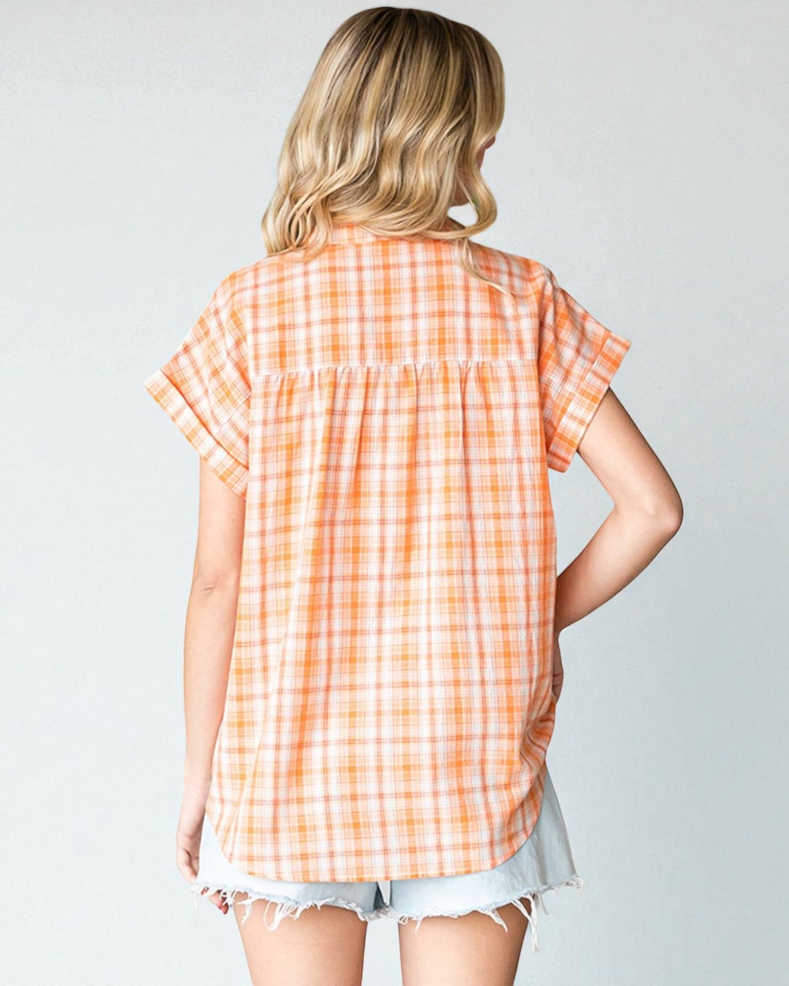 Woman wearing an orange and white checkered shirt against a plain background