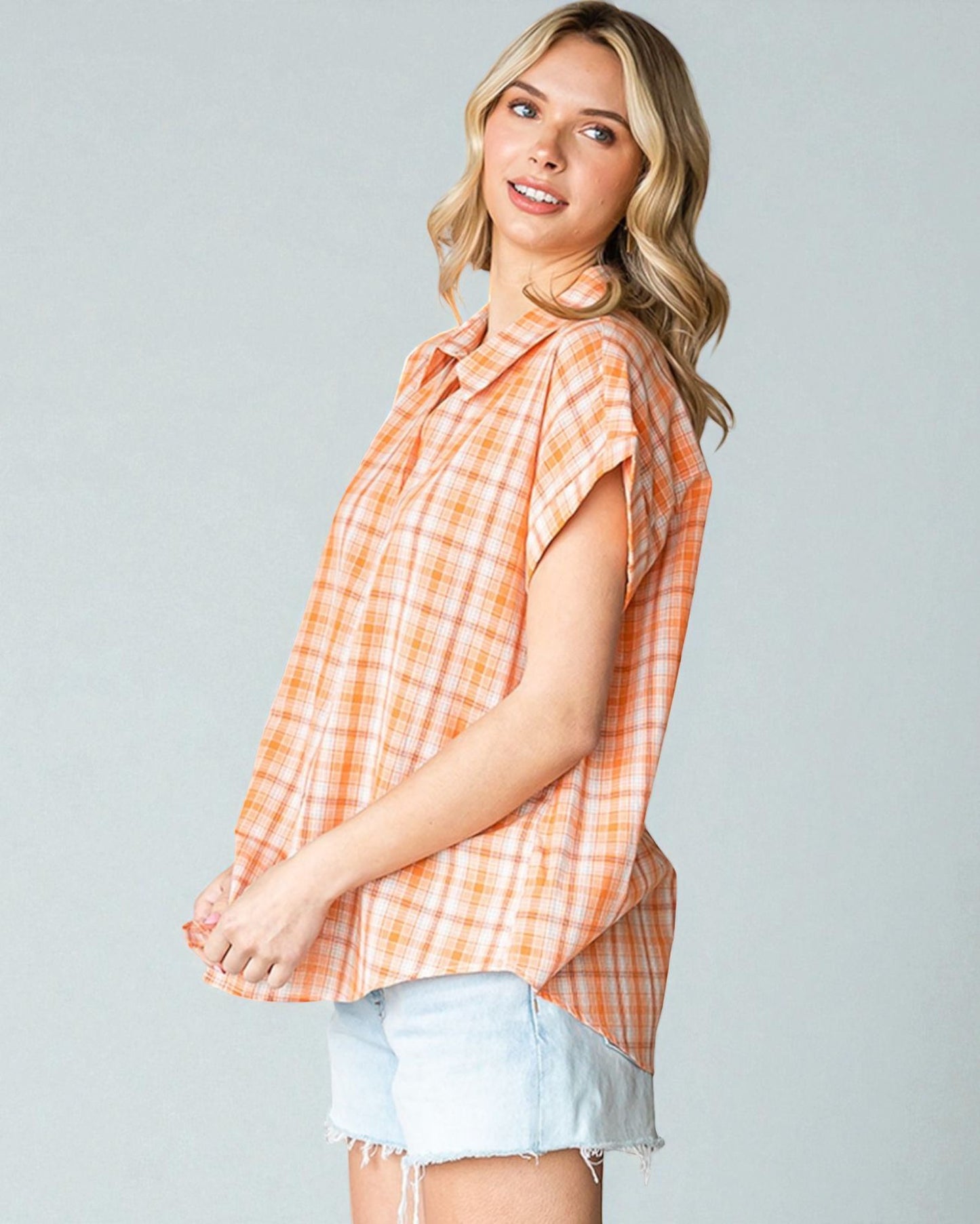 Woman wearing an orange plaid shirt and denim shorts on a gray background