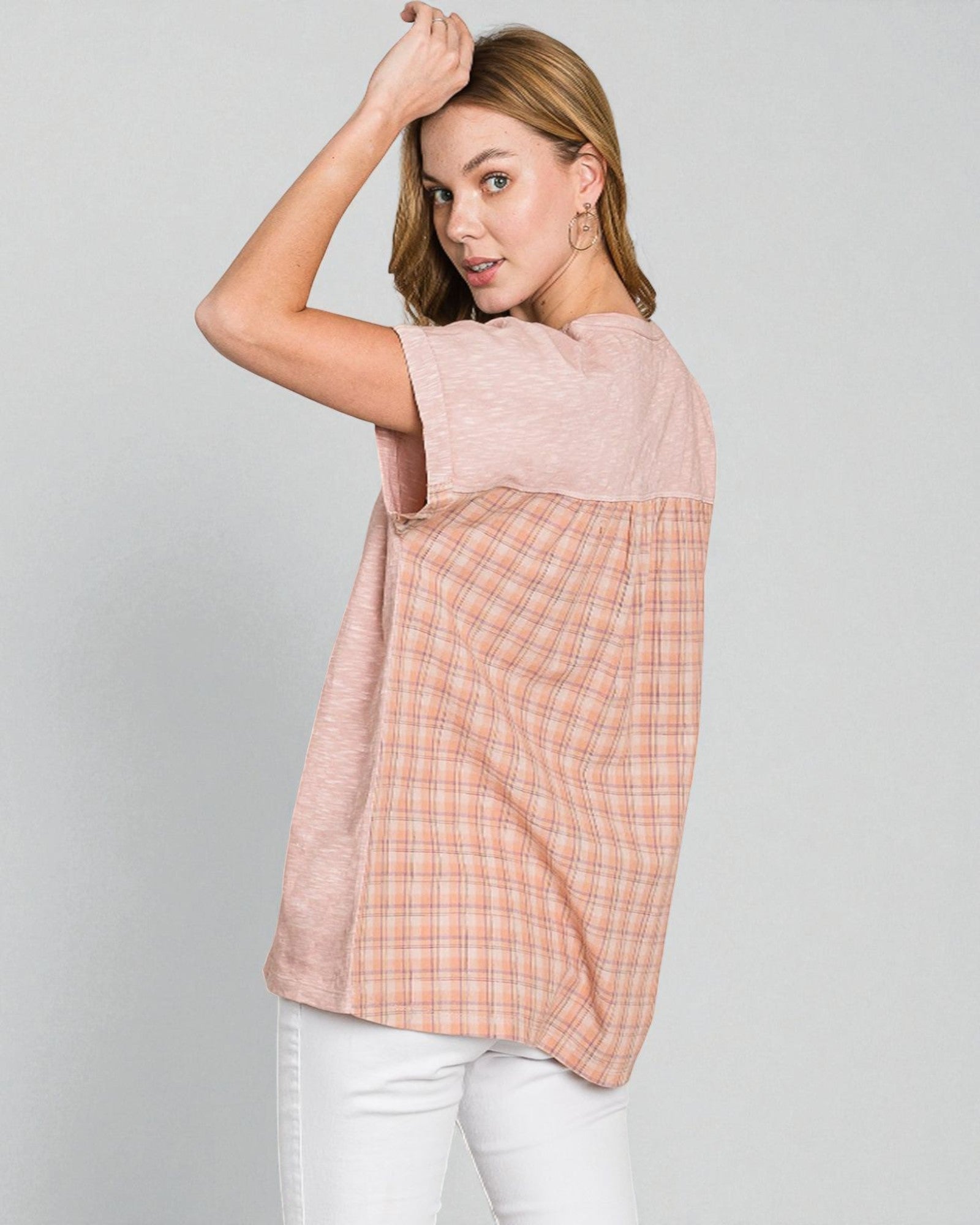 Woman wearing a sleeveless pink and plaid top on a gray background