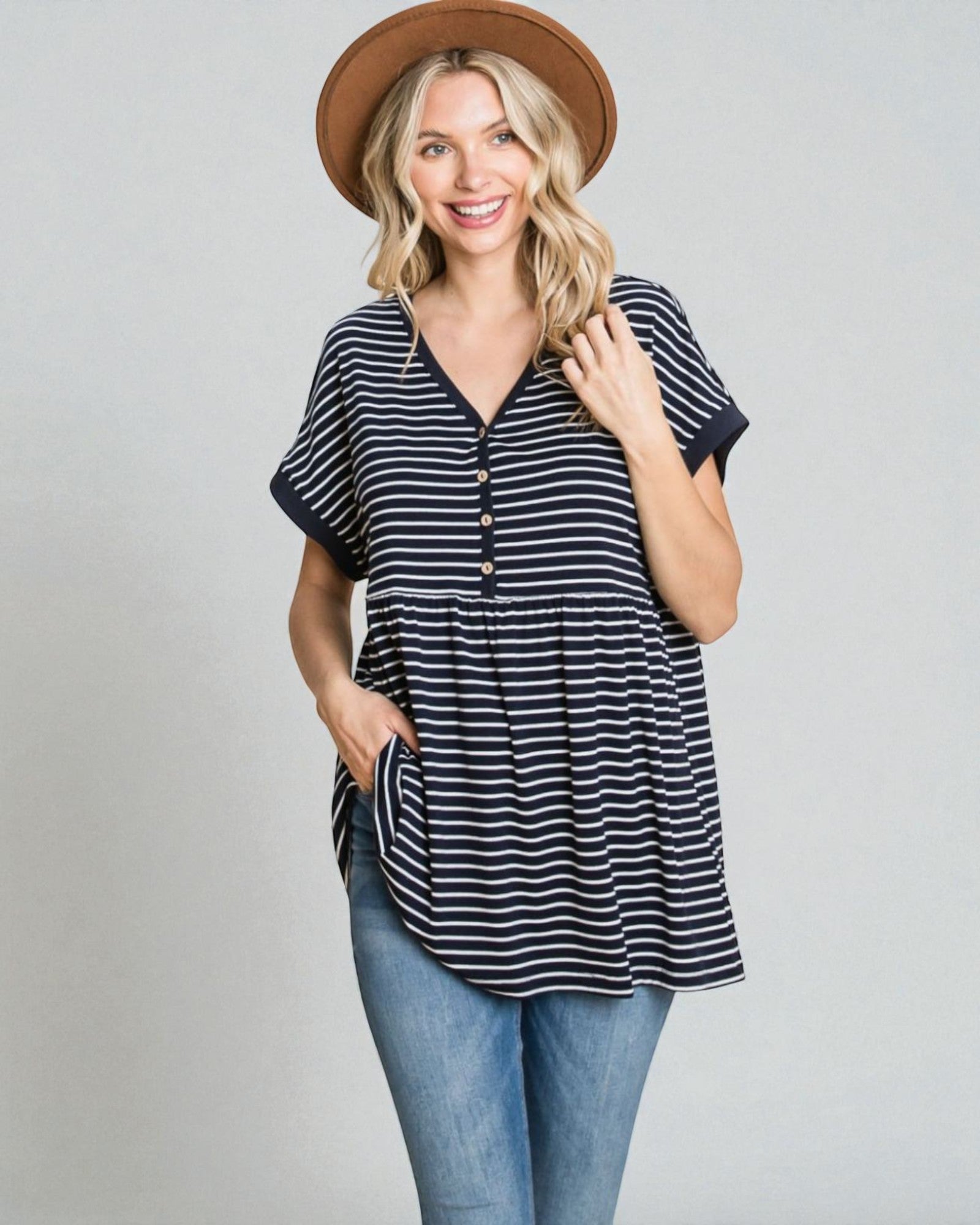 Woman wearing a striped shirt, jeans, and a hat on a plain background