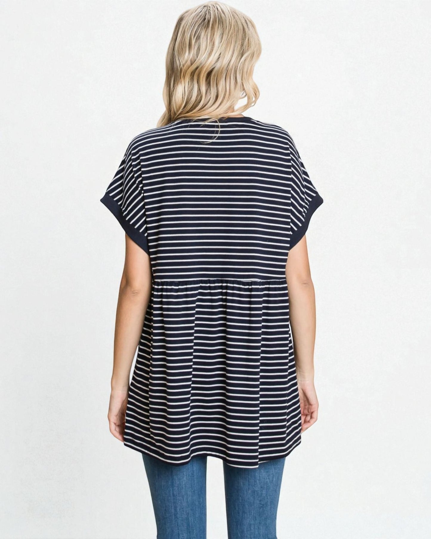 Woman wearing a black and white striped tunic with blue jeans on a light gray background