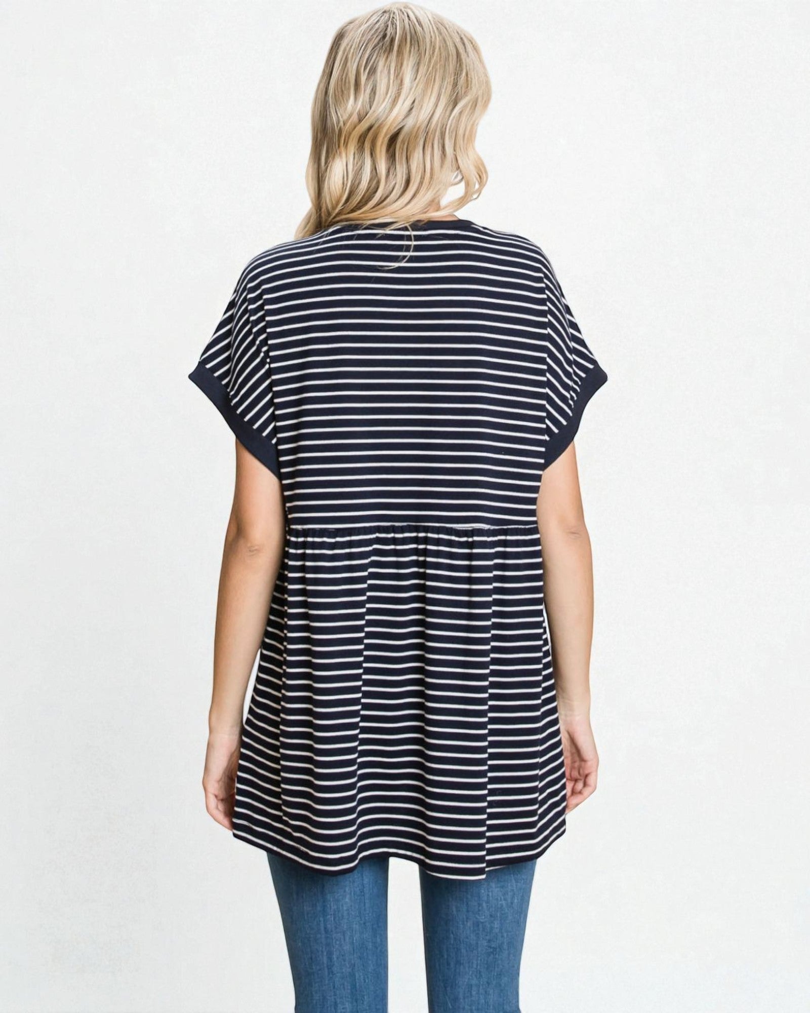 Woman wearing a black and white striped tunic with blue jeans on a light gray background