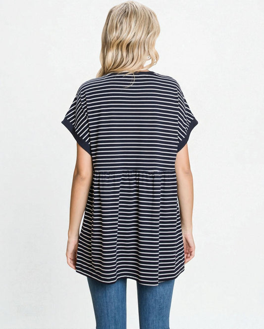 Woman wearing a black and white striped tunic with blue jeans on a light gray background