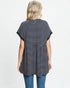 Woman wearing a black and white striped tunic with blue jeans on a light gray background