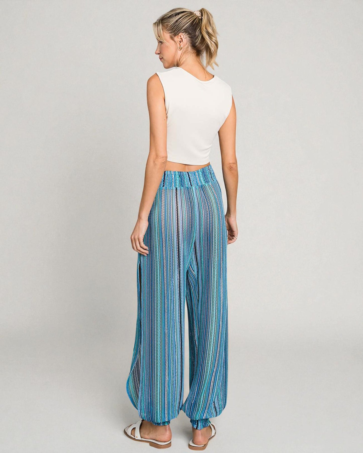 Woman wearing a white sleeveless top and blue striped pants on a gray background