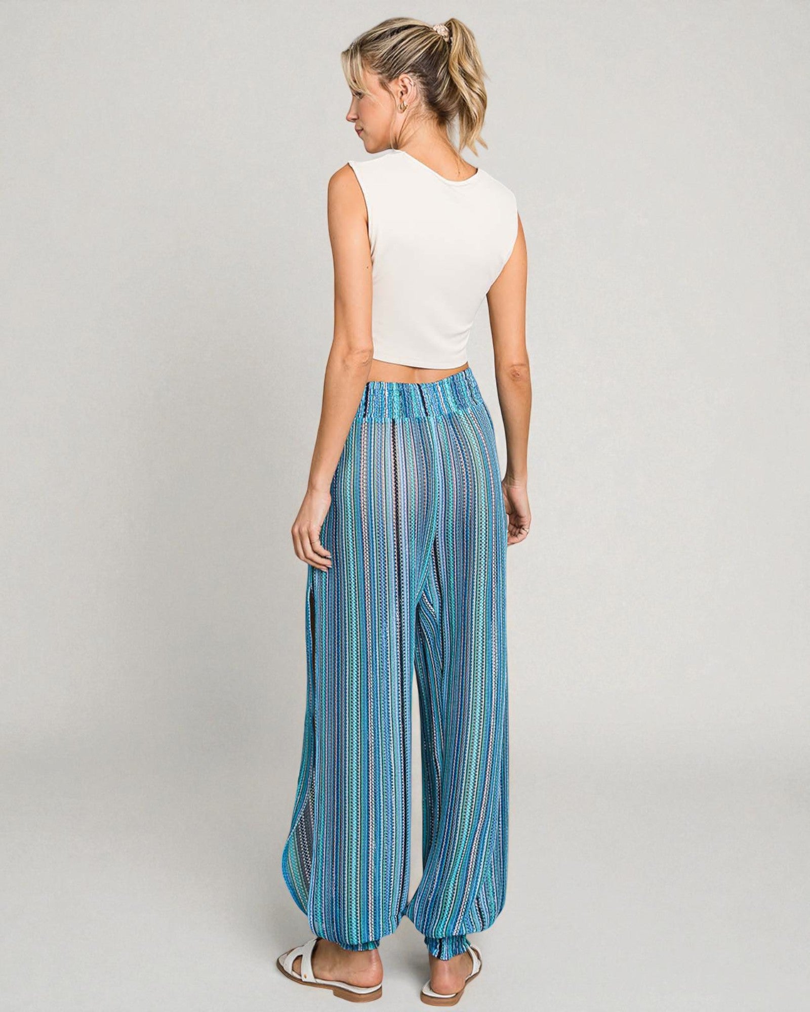 Woman wearing a white sleeveless top and blue striped pants on a gray background