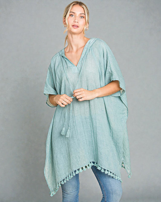 Woman wearing a light blue poncho with pom-pom trim on a gray background