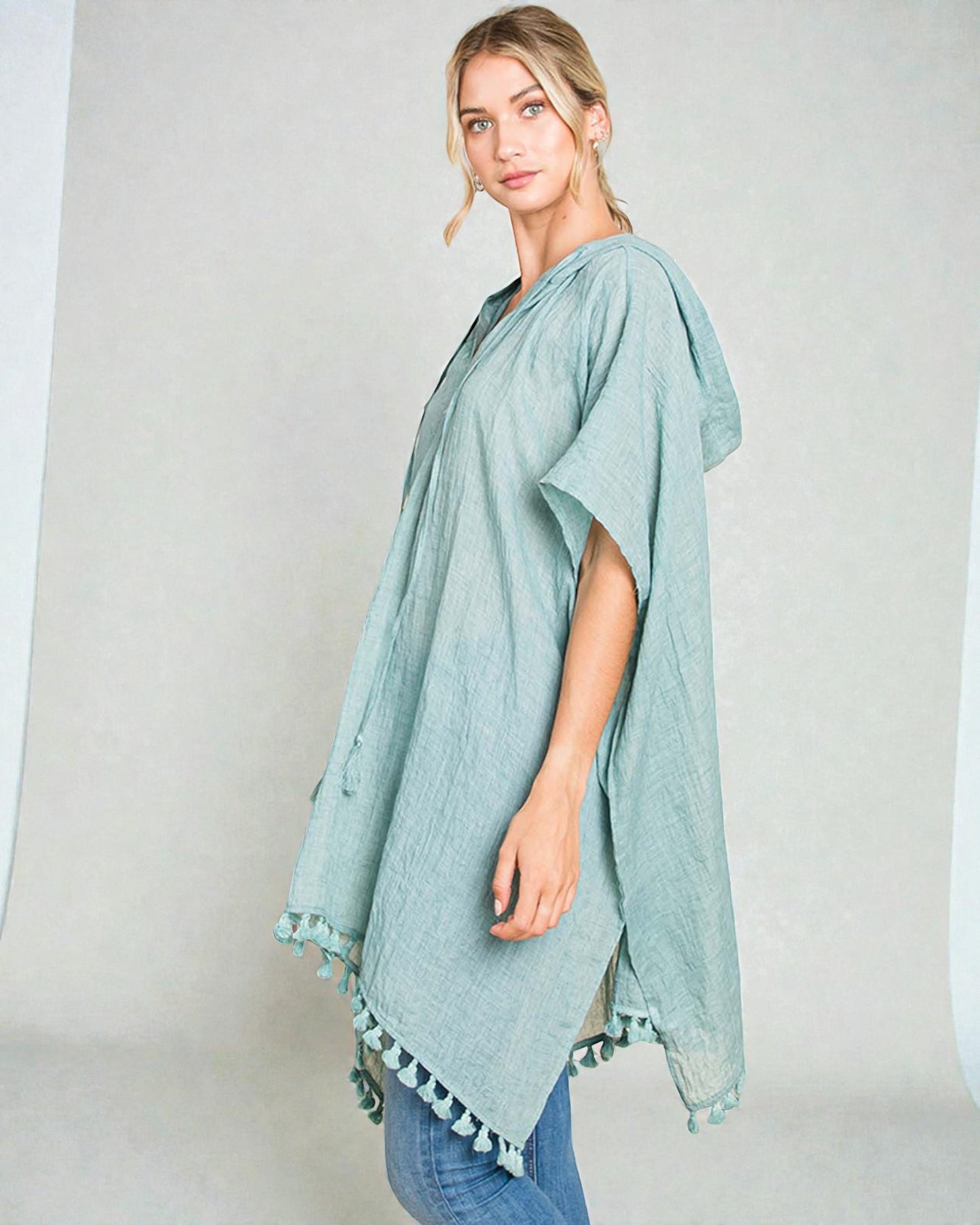 Woman wearing a light blue poncho with tassels on a plain background