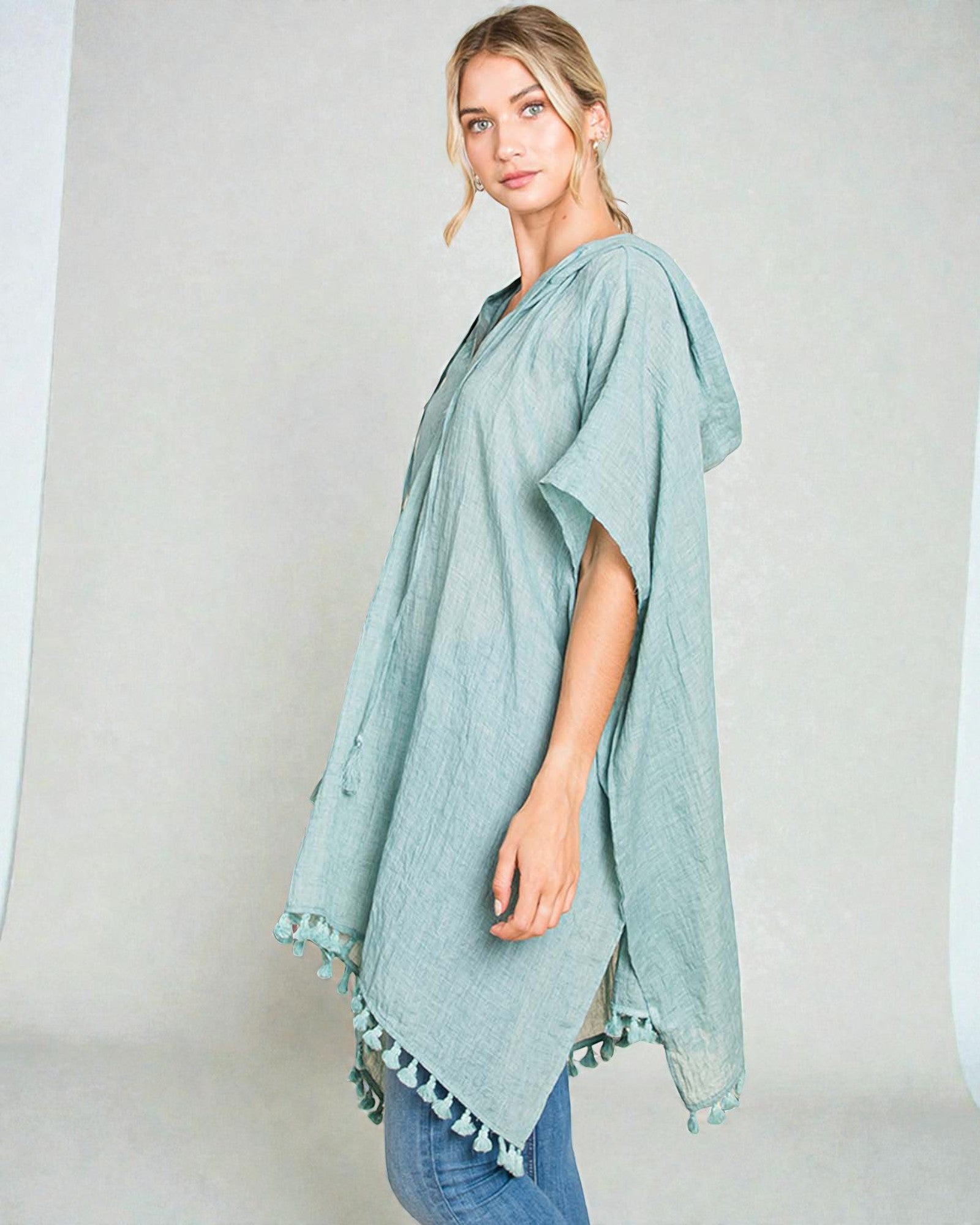 Woman wearing a light blue poncho with tassels on a plain background