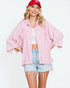 Woman wearing a pink kimono-style shirt, denim shorts, and a red cap on a white background