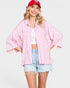 Woman wearing a pink patterned shirt, white crop top, and denim shorts with a red cap on a light gray background