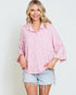 Woman wearing a pink patterned shirt and denim shorts against a white background