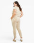 A woman modeling a beige short-sleeve wrap-style top and matching slim-fit pants, shown from the back against a plain light gray studio background.
