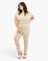 A woman modeling a beige two-piece lounge set consisting of a short-sleeve crewneck top and matching drawstring pants, paired with white platform wedge sandals, against a plain white studio background.