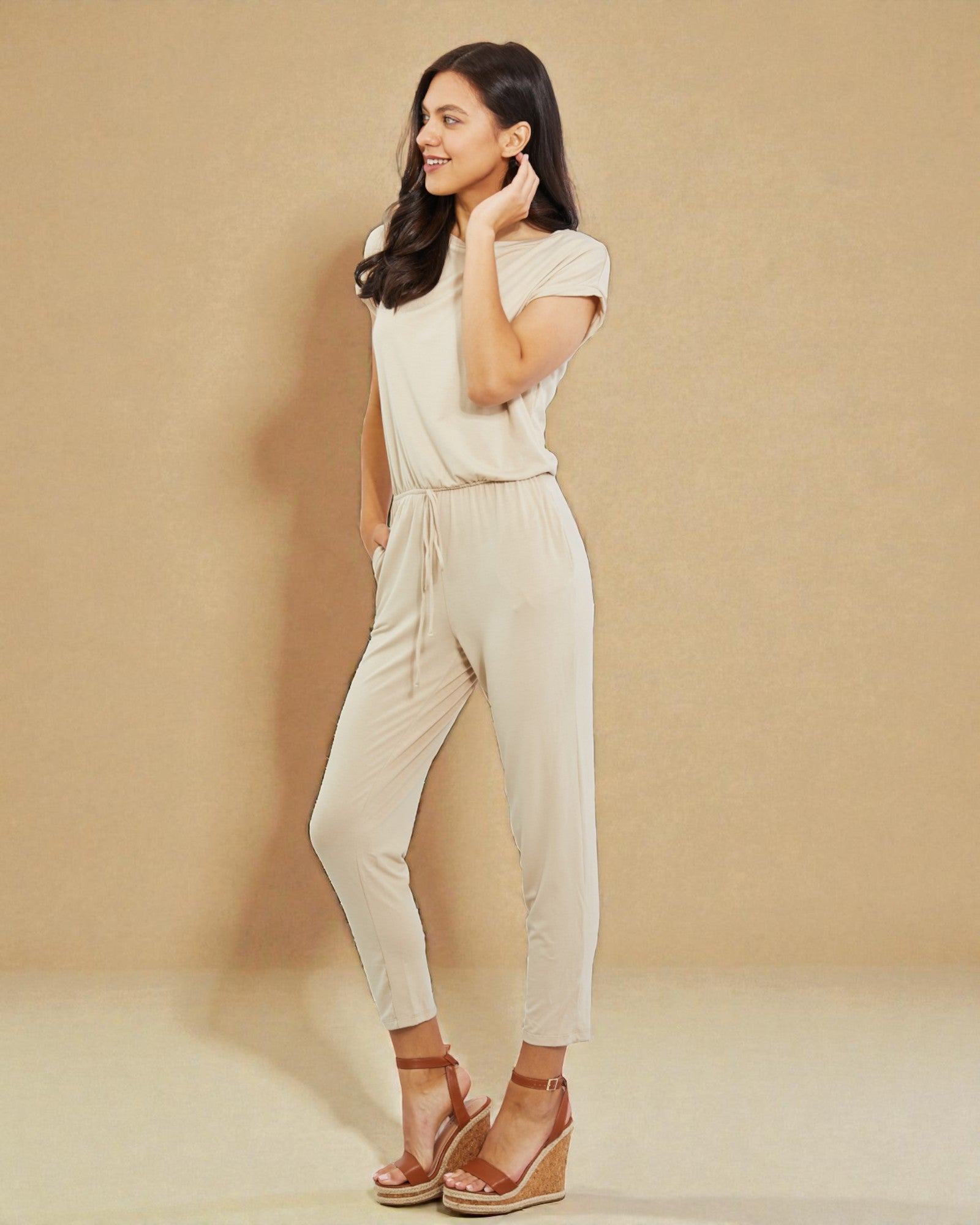 Woman wearing a beige jumpsuit against a beige background