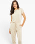 A woman modeling a light beige short-sleeve jumpsuit with a drawstring waist and side pockets, photographed against a clean white studio background.