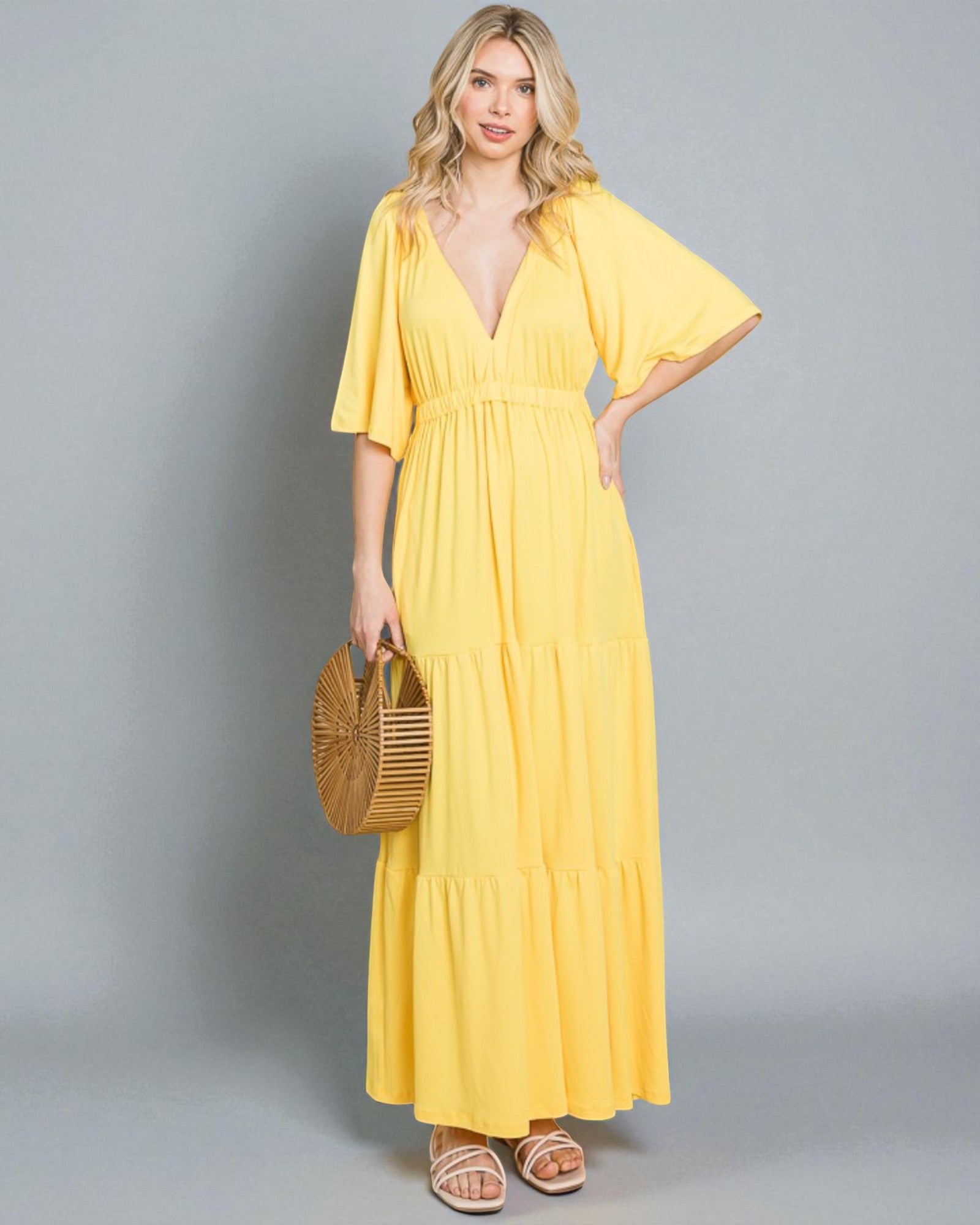 Woman wearing a yellow dress holding a straw bag on a gray background