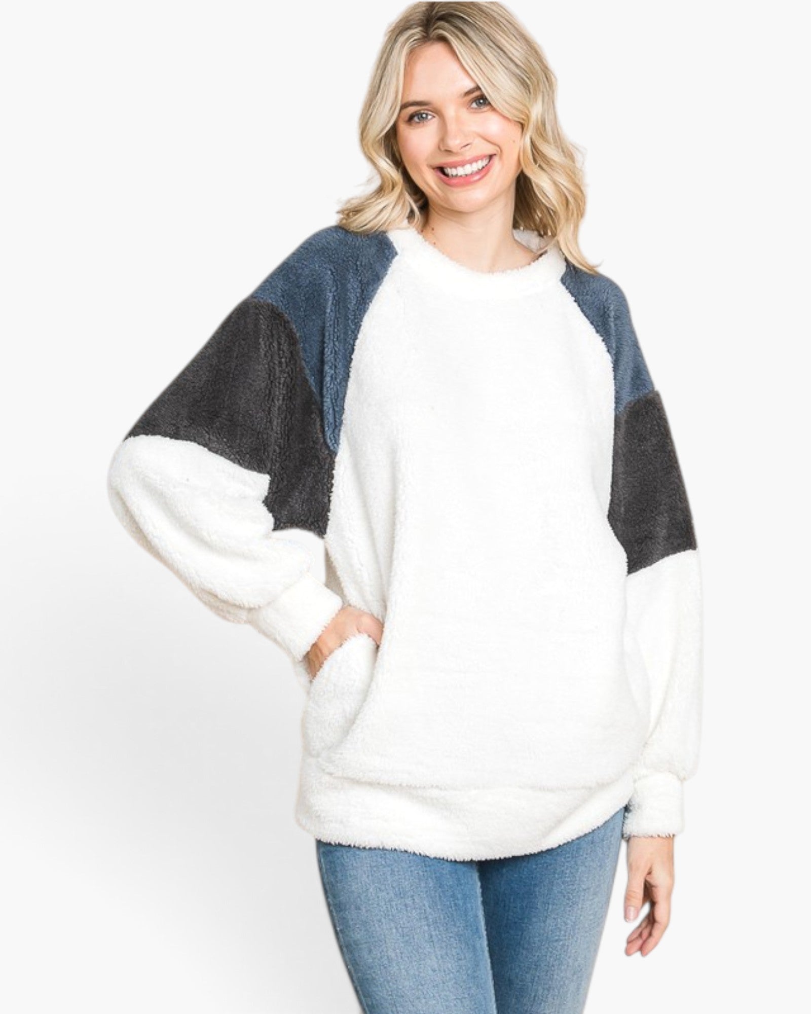 A woman wearing a fuzzy colorblock pullover sweater with a white body, dark gray sleeves, and blue-gray shoulder panels, paired with blue jeans, against a plain white background.