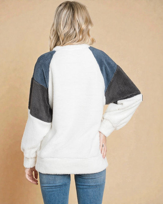 Person wearing a color-blocked sweater with white, blue, and black sleeves on a beige background