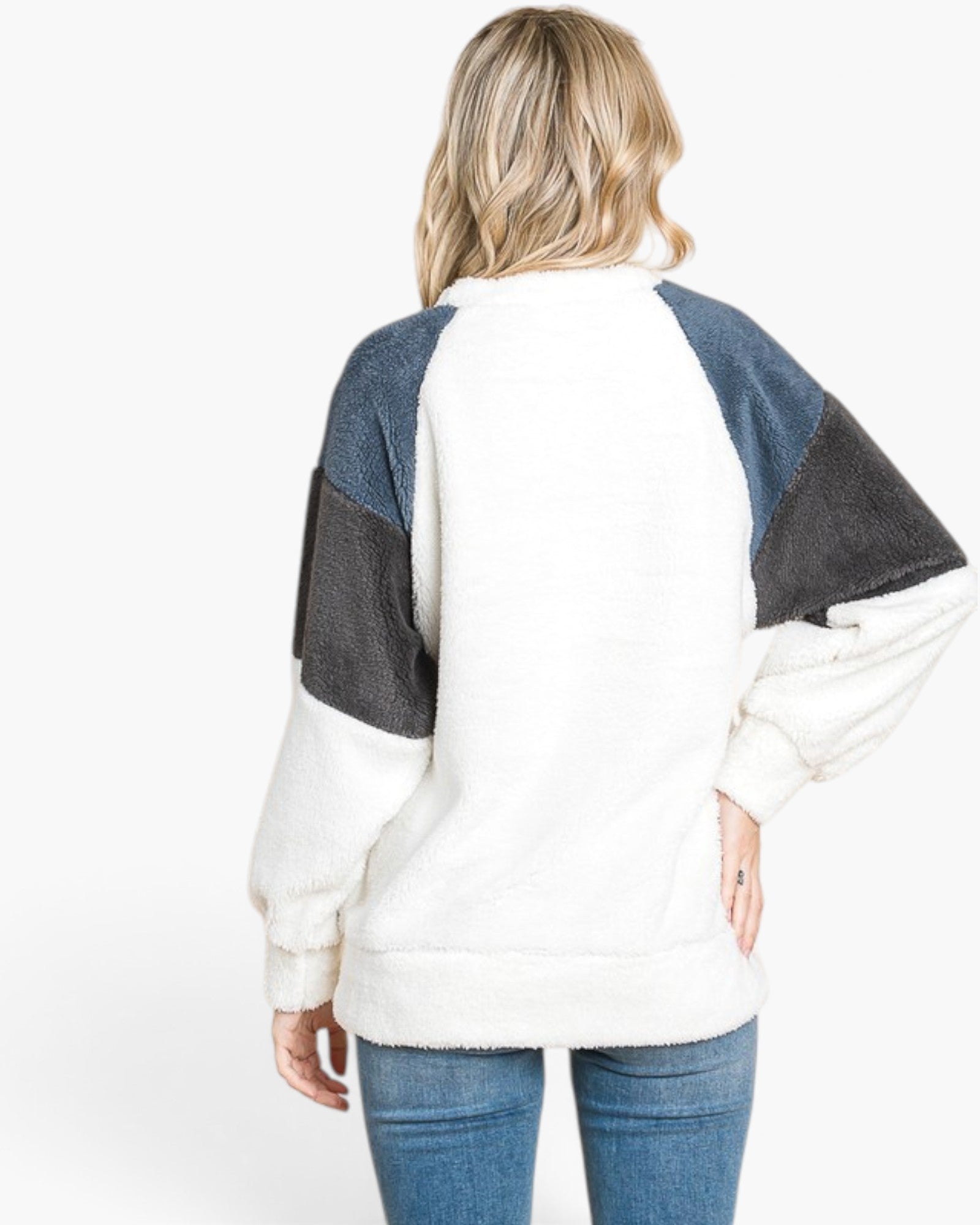 A woman viewed from the back wearing a fuzzy color-block sweatshirt with a white body, blue denim shoulder panels, and dark charcoal sleeve panels, paired with blue jeans against a plain white background.