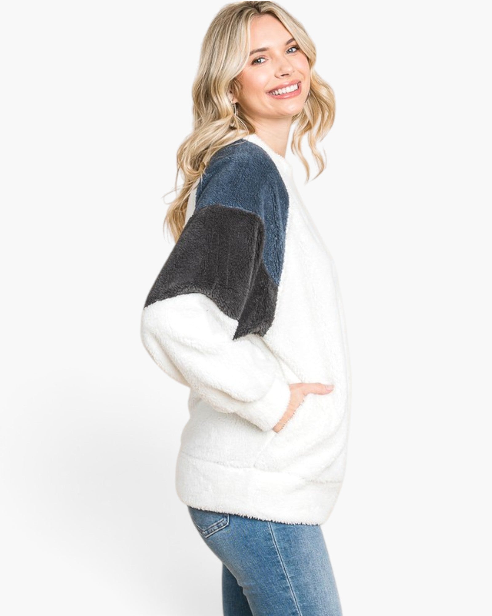 A woman wearing a fuzzy color-block knit sweater with a white body, a dark blue shoulder panel, and a dark charcoal sleeve panel, paired with blue jeans, against a plain white background.