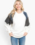 A woman wearing a color-blocked colorblock fleece pullover sweater with a white body, dark gray sleeves, and navy blue shoulder panels, paired with blue jeans, against a plain white studio background.