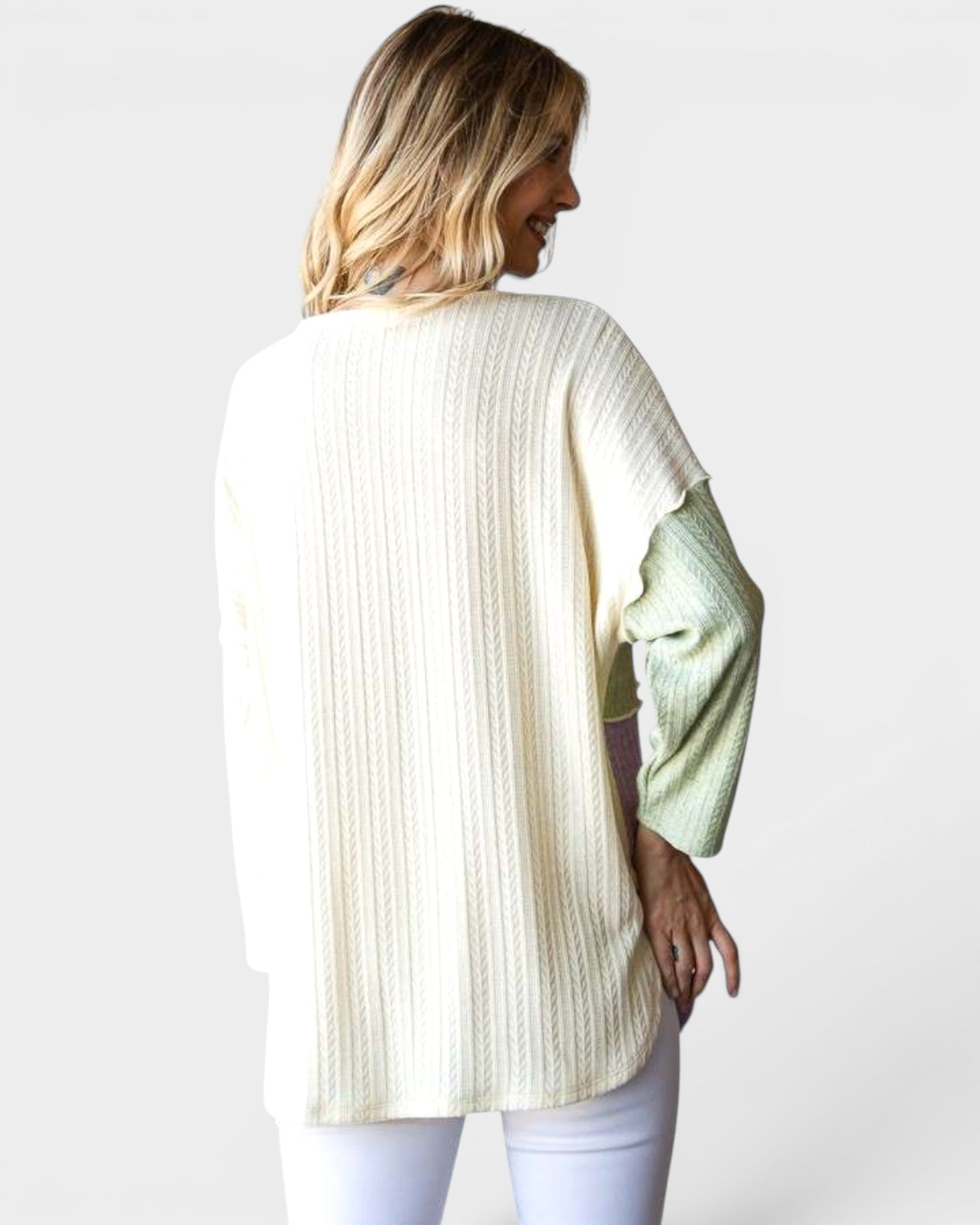 Woman wearing a cream-colored sweater with a light green sleeve on a white background