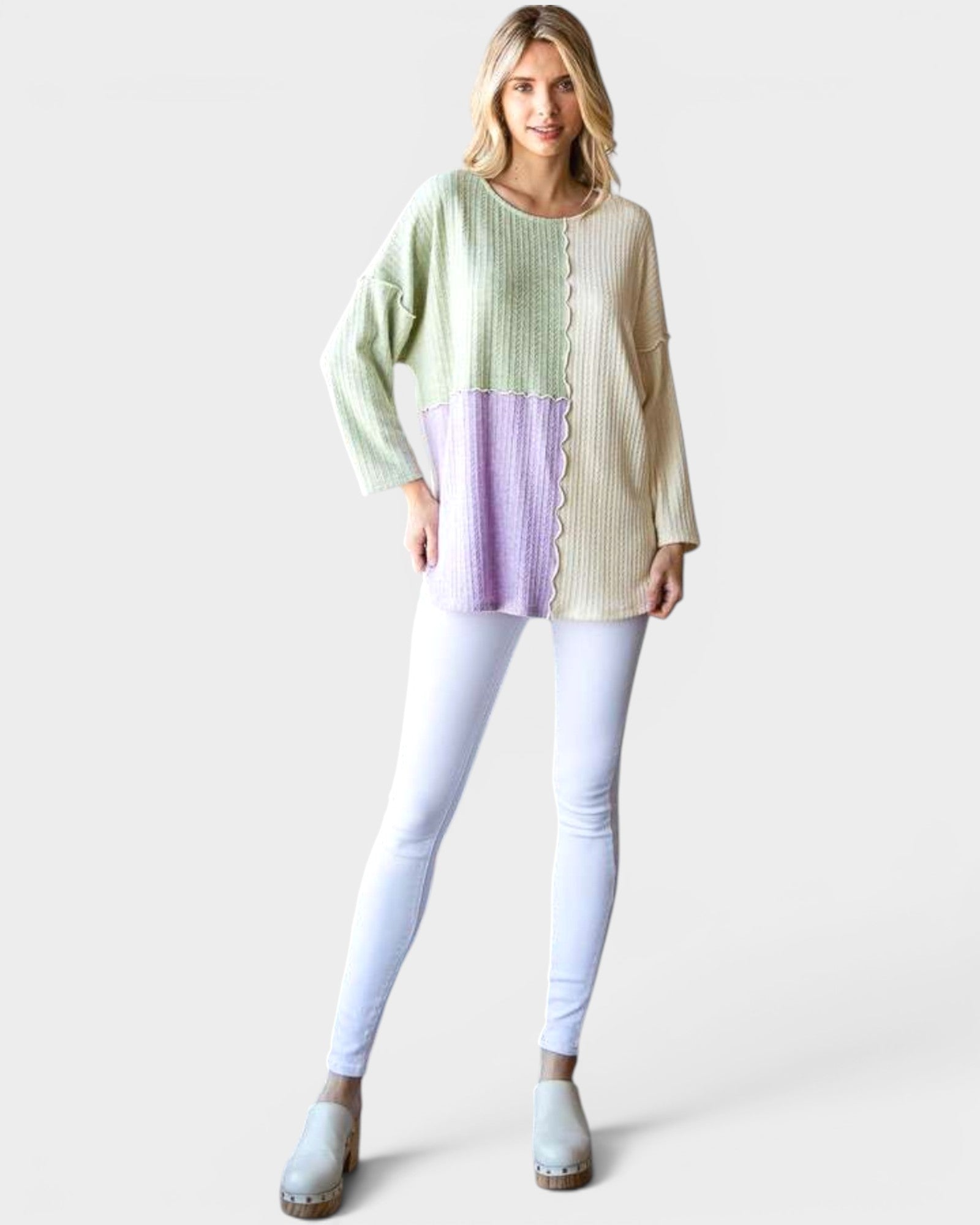 Woman wearing a pastel color-blocked sweater and light gray pants on a white background