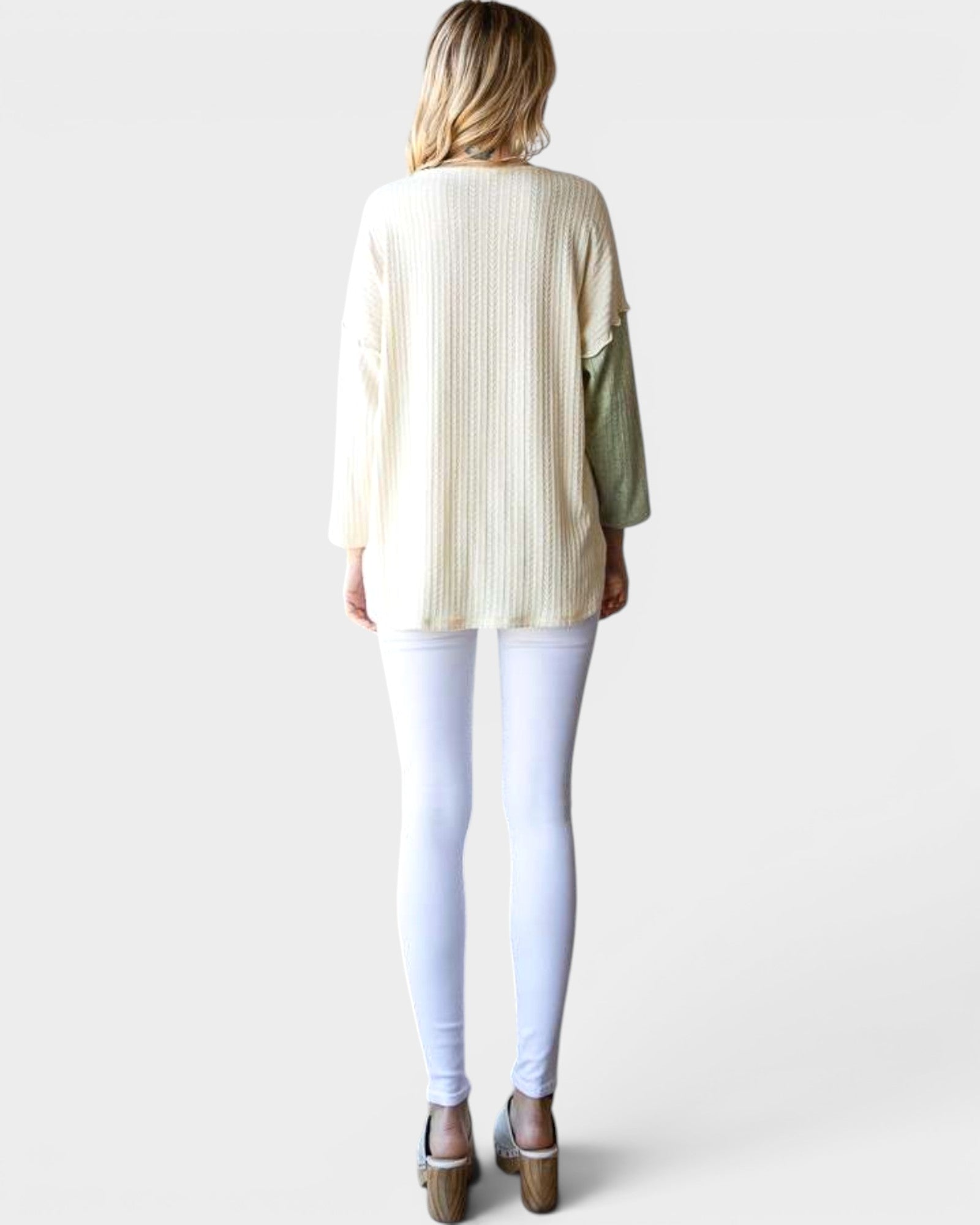 Woman wearing a cream-colored blouse with a green sleeve and white pants on a plain background