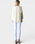 Woman wearing a cream-colored blouse with a green sleeve and white pants on a plain background