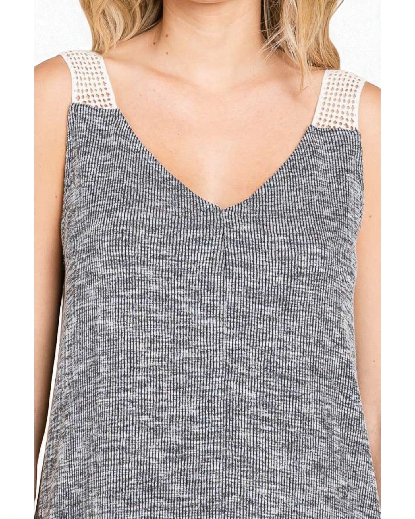 Close-up of a sleeveless top with textured pattern and white lace trim on a plain background