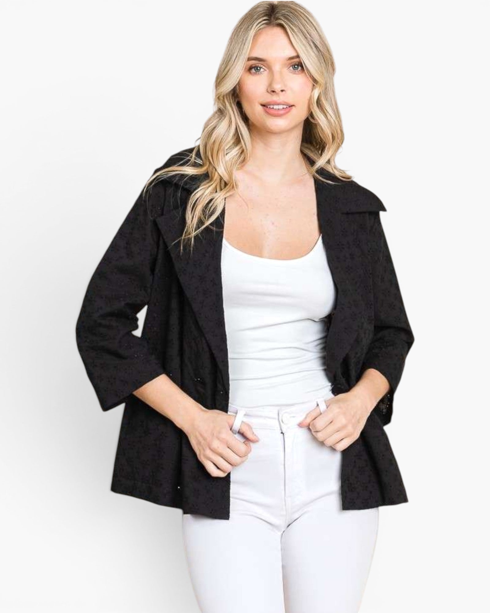 A woman modeling a black textured open-front jacket over a white tank top and white pants, photographed against a clean white studio background.
