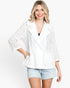 A woman wearing a white eyelet lace blazer with a collar and three-quarter sleeves, paired with light-wash denim shorts, against a plain white studio background.