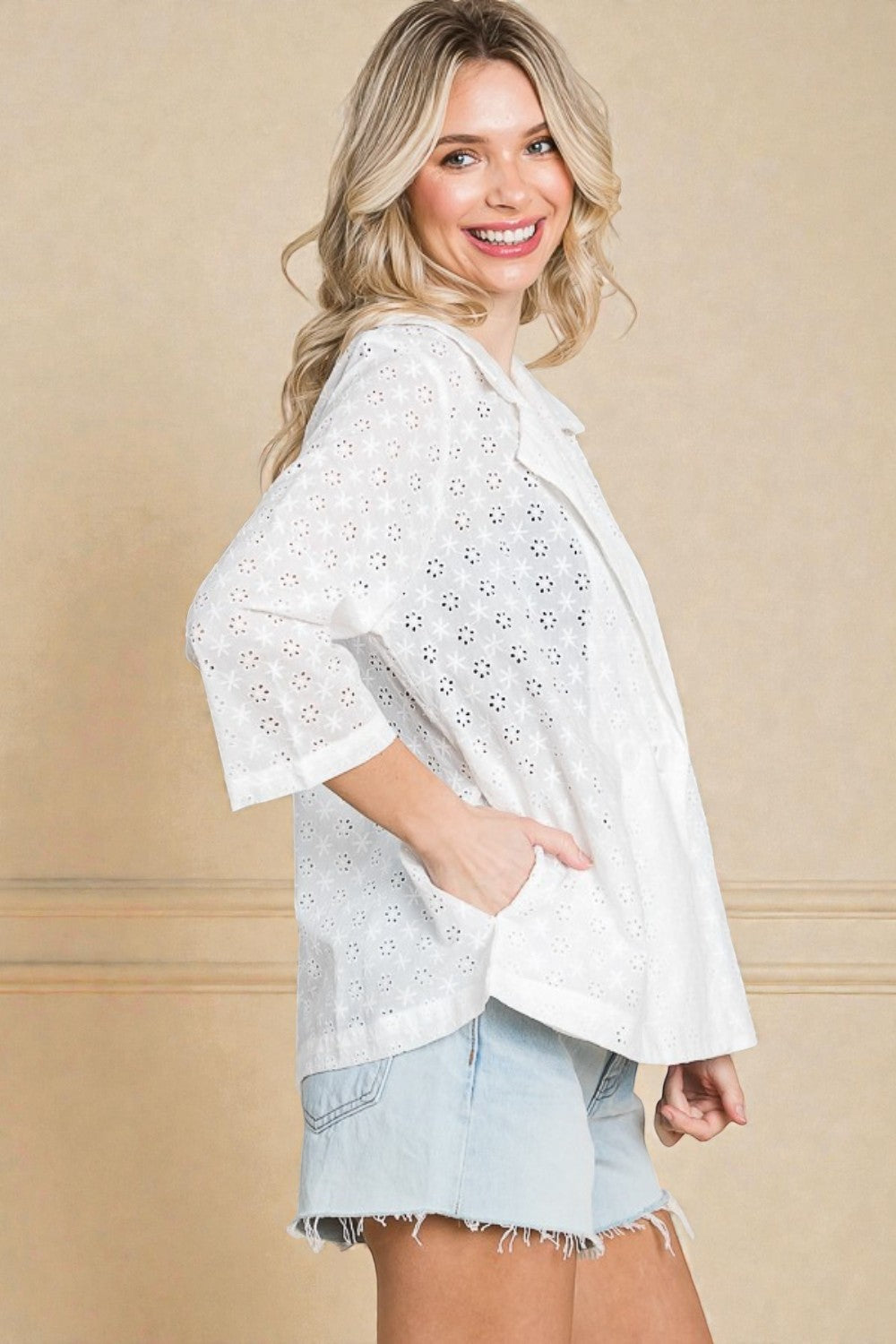 Woman wearing a white lace top and denim shorts against a beige background