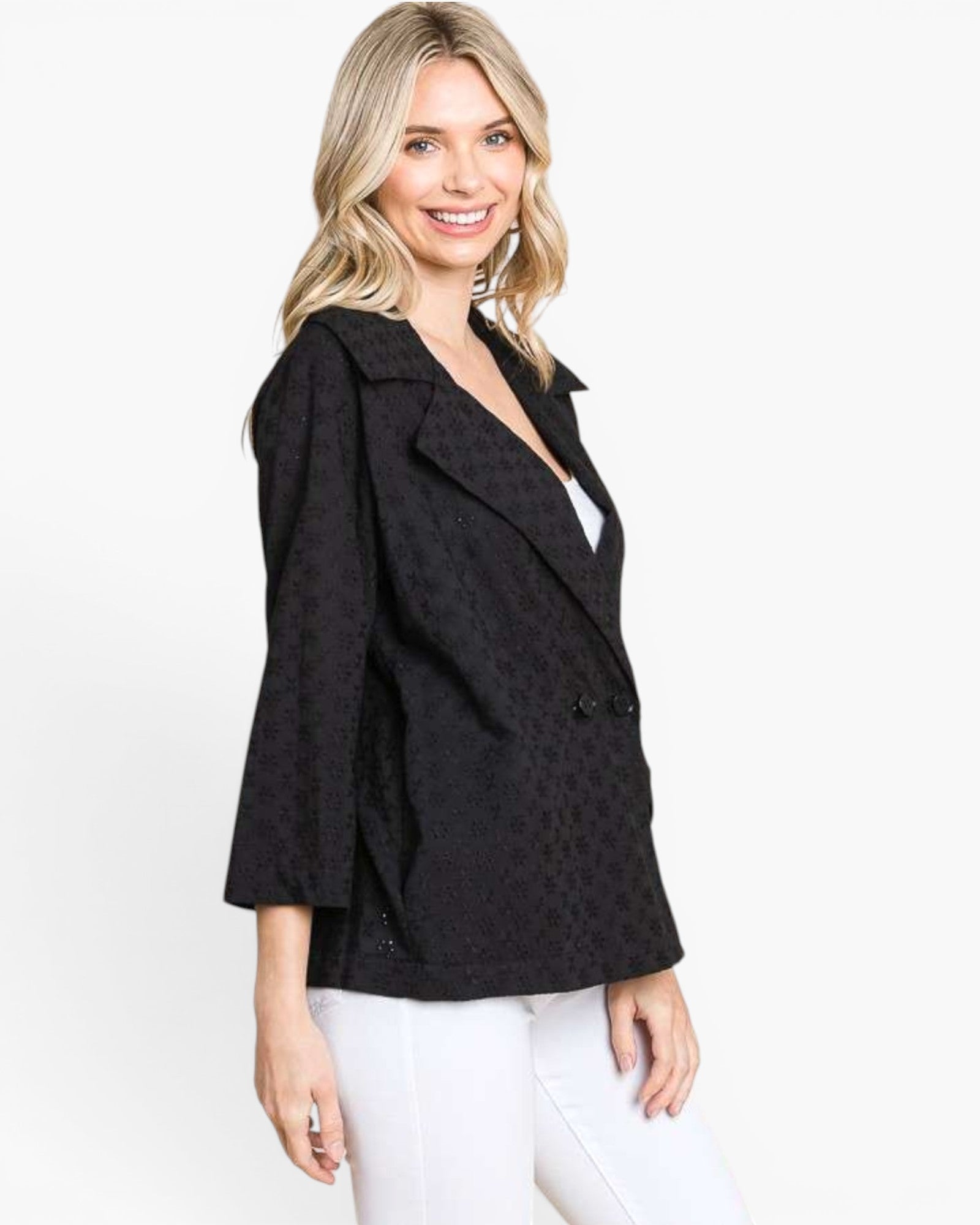 A woman modeling a black textured blazer with three-quarter sleeves and a double-breasted front, paired with white pants, against a plain white studio background.
