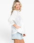 A woman wearing a white eyelet button-up shirt and light-wash denim shorts, photographed against a clean white studio background.