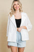 Woman wearing a white lace jacket over a black top and denim shorts on a beige background