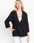 A woman wearing a black textured double-breasted blazer with three-quarter sleeves over a white top and white pants, photographed against a clean white studio background.