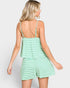 A woman modeling a light green and white striped romper with side pockets, set against a plain light gray background.