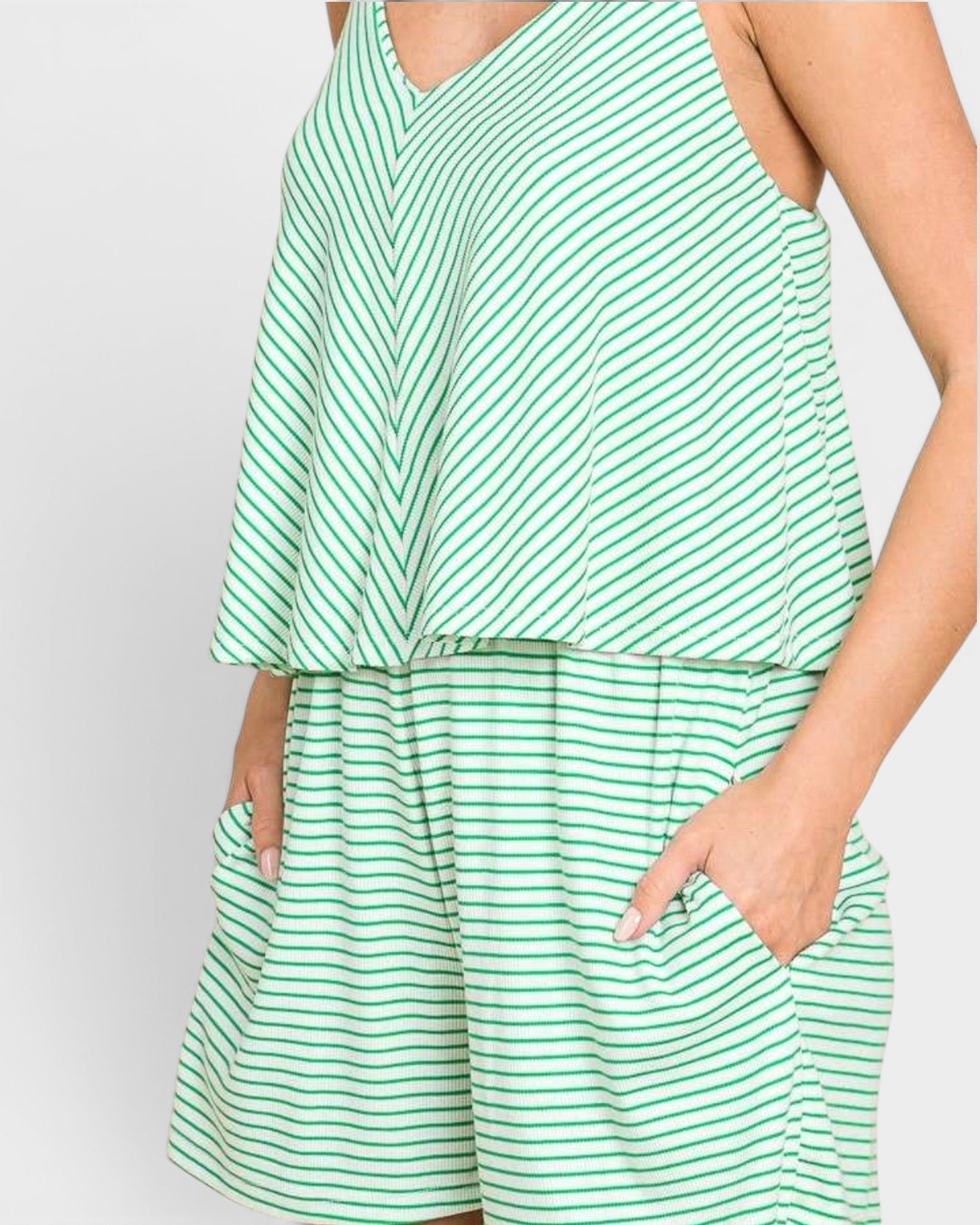 A close-up of a model wearing a green and white striped sleeveless romper with a V-neckline and side pockets.