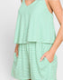 A close-up of a model wearing a green and white striped sleeveless romper with a V-neckline and side pockets.