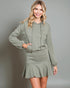 Woman wearing a green hoodie and skirt set against a gray background