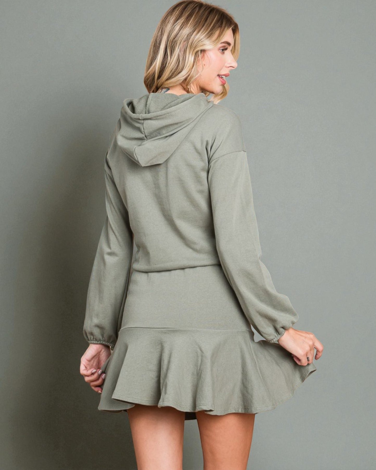 Woman wearing a green hoodie and skirt set against a gray background