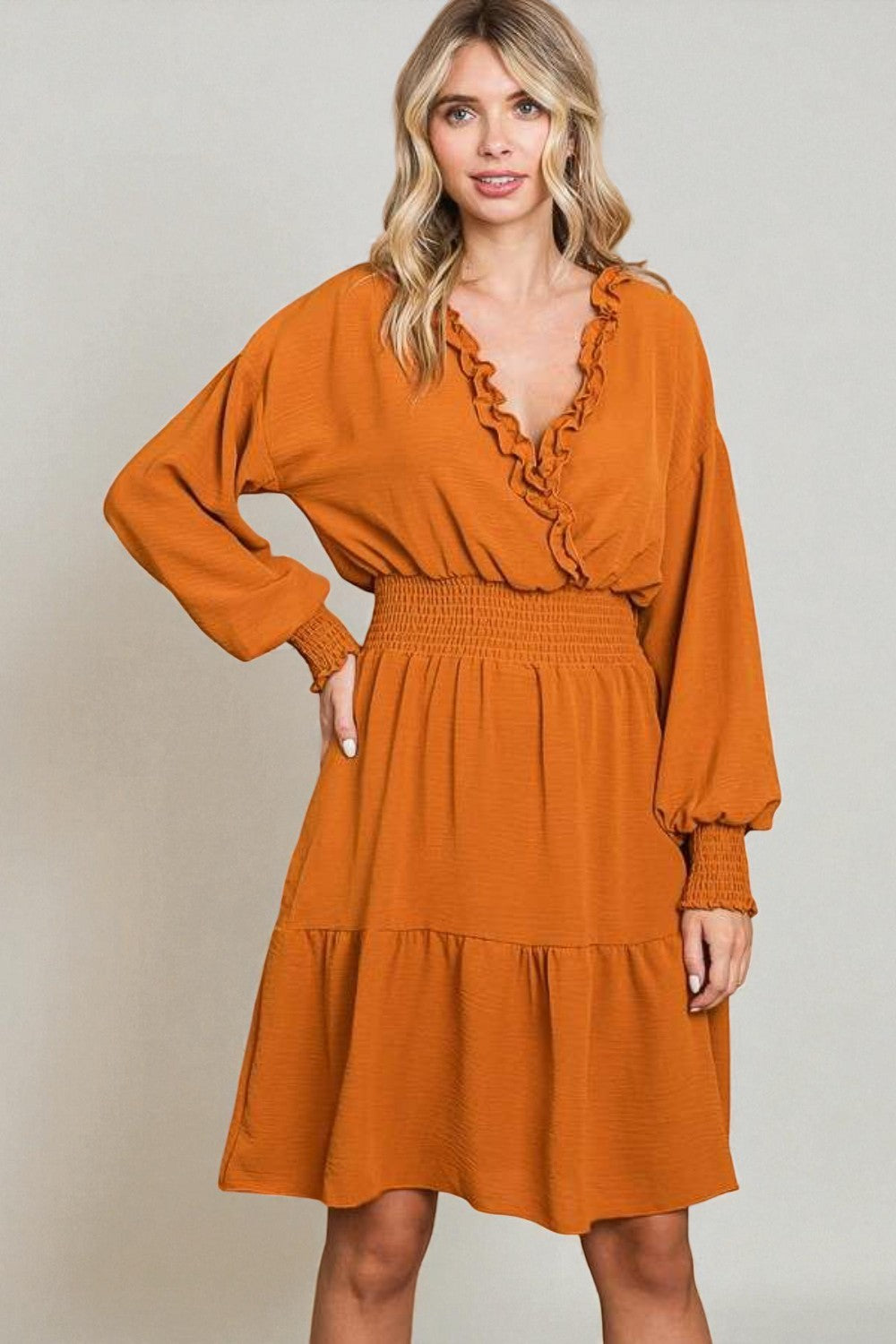 Woman wearing a rust-colored dress with long sleeves against a plain background