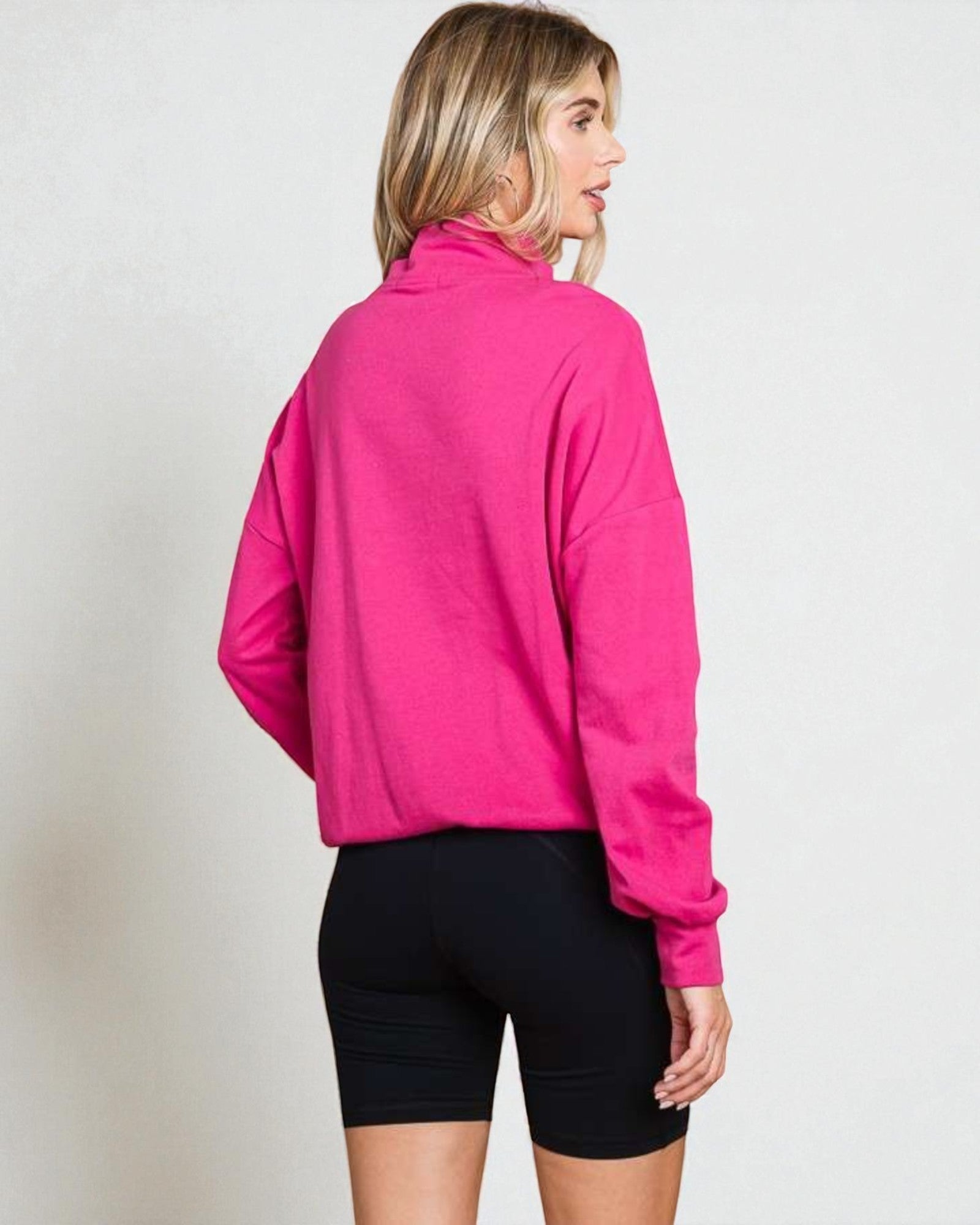 Person wearing a bright pink jacket and black shorts on a plain background