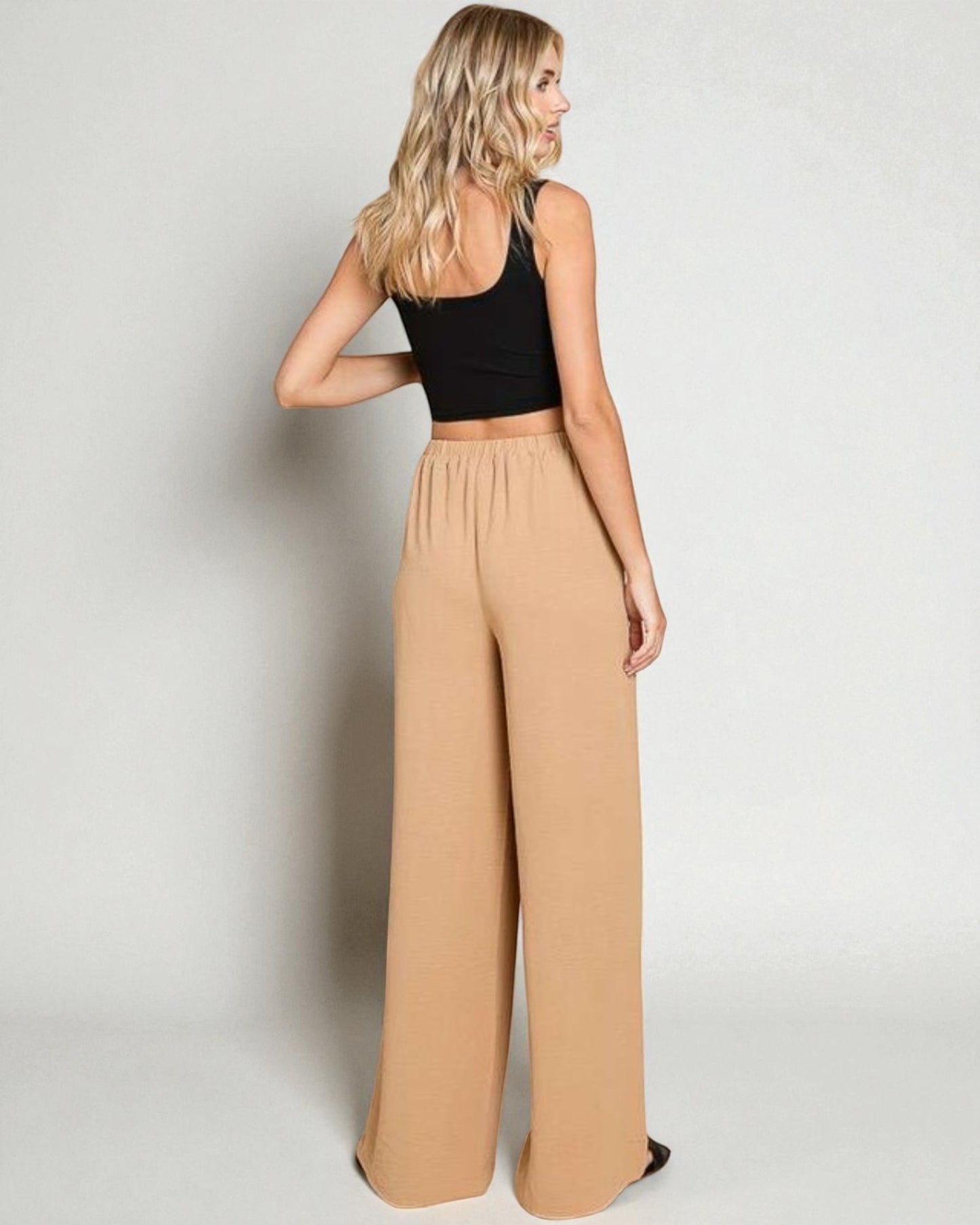 Woman wearing a black top and beige wide-leg pants on a plain background
