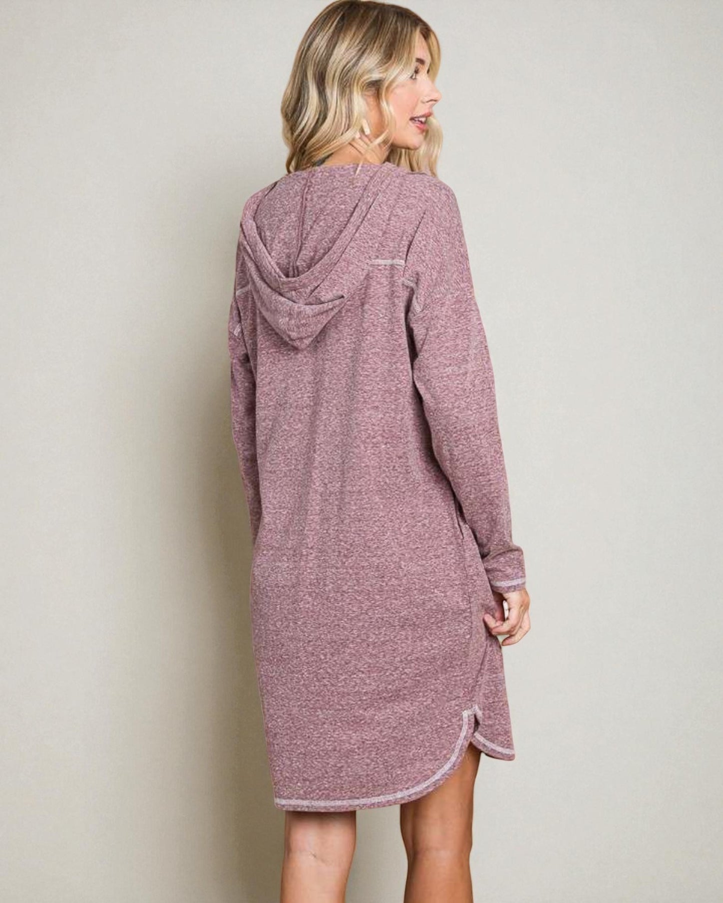 Woman wearing a mauve hooded dress against a plain background